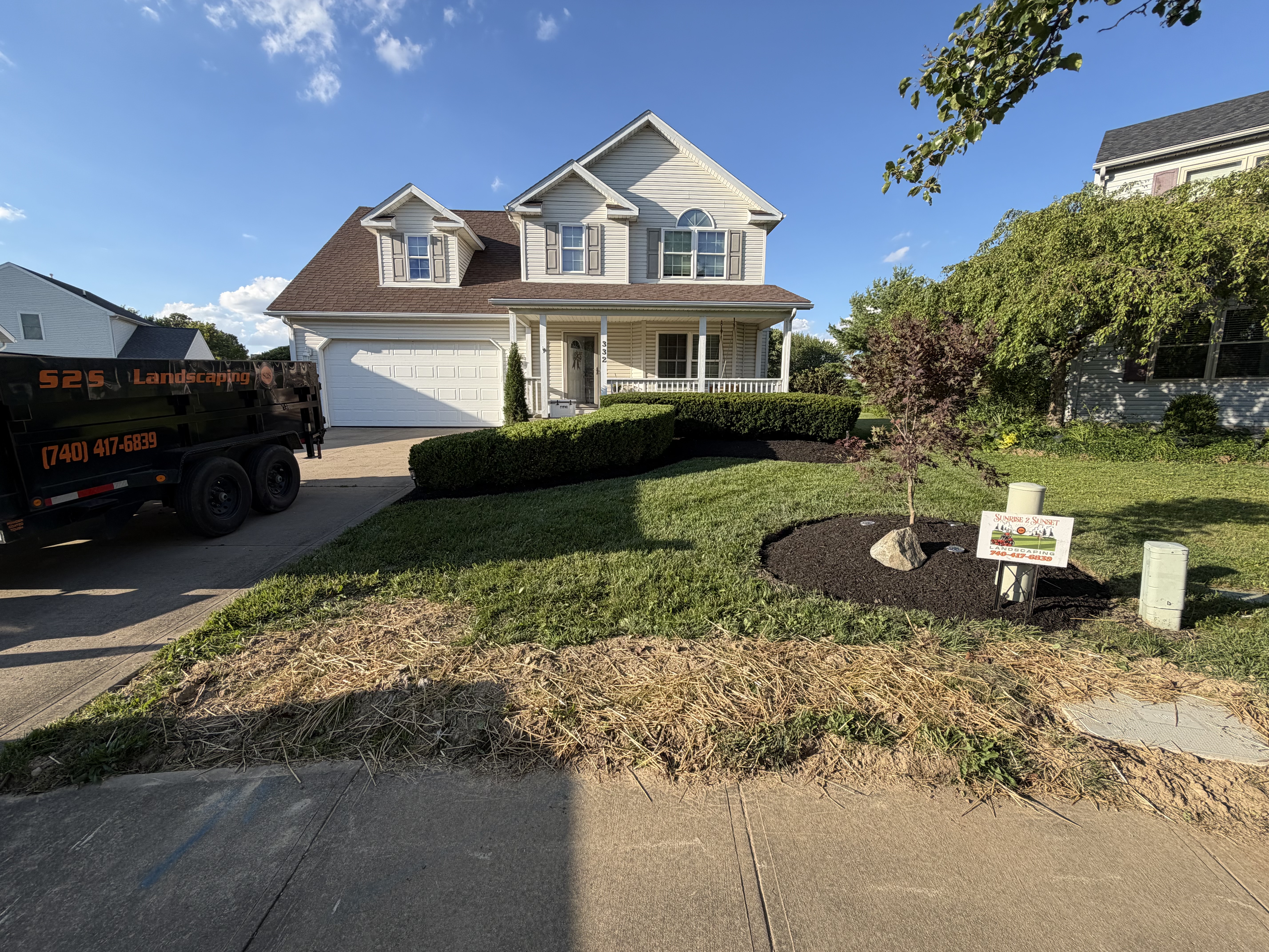 Front yard with manicured hedges, dark mulch beds, and fresh grass turf next to a work truck