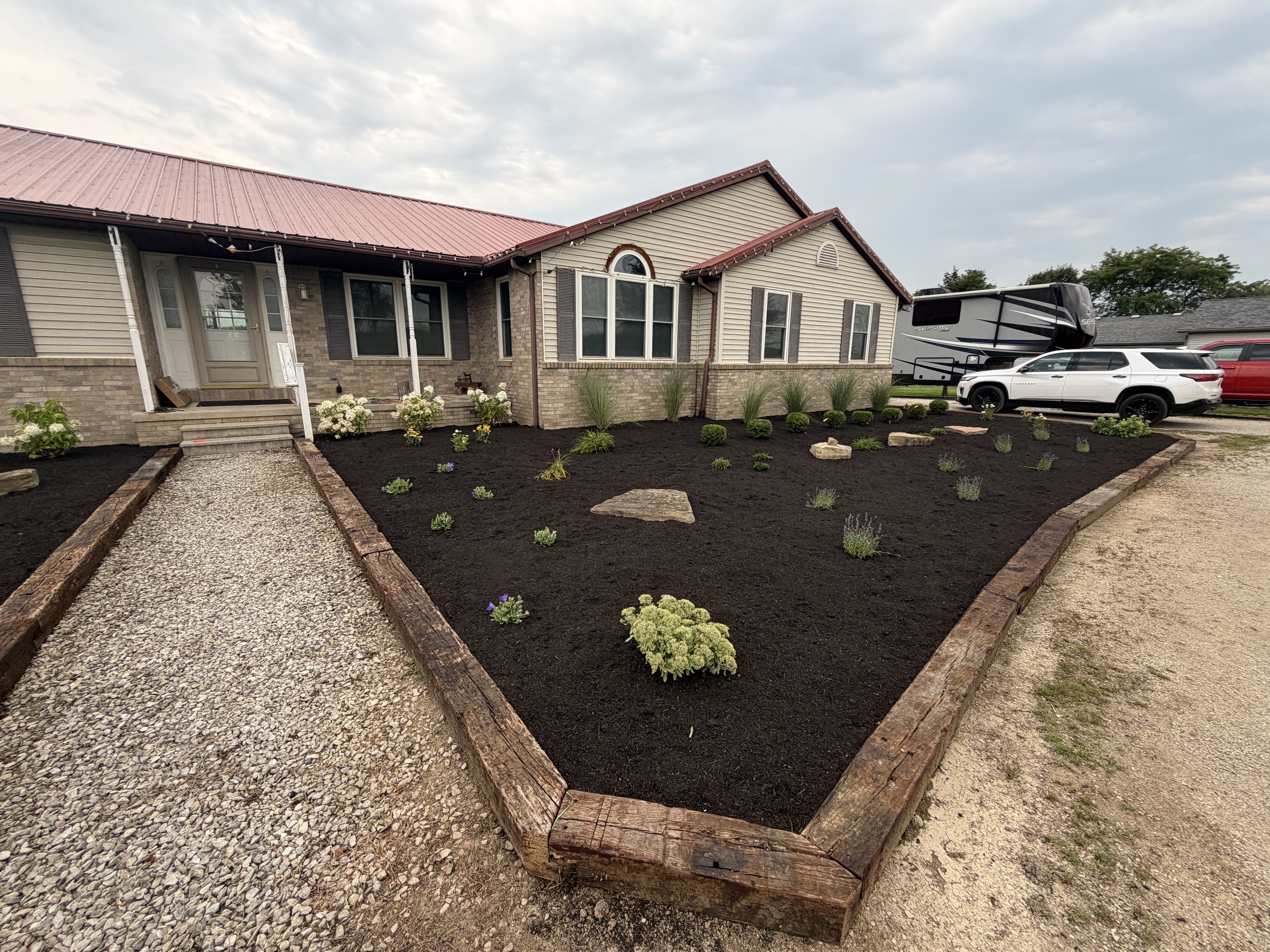 Freshly mulched front garden bed enclosed by heavy timber borders with newly planted flowers and ornamental grasses
