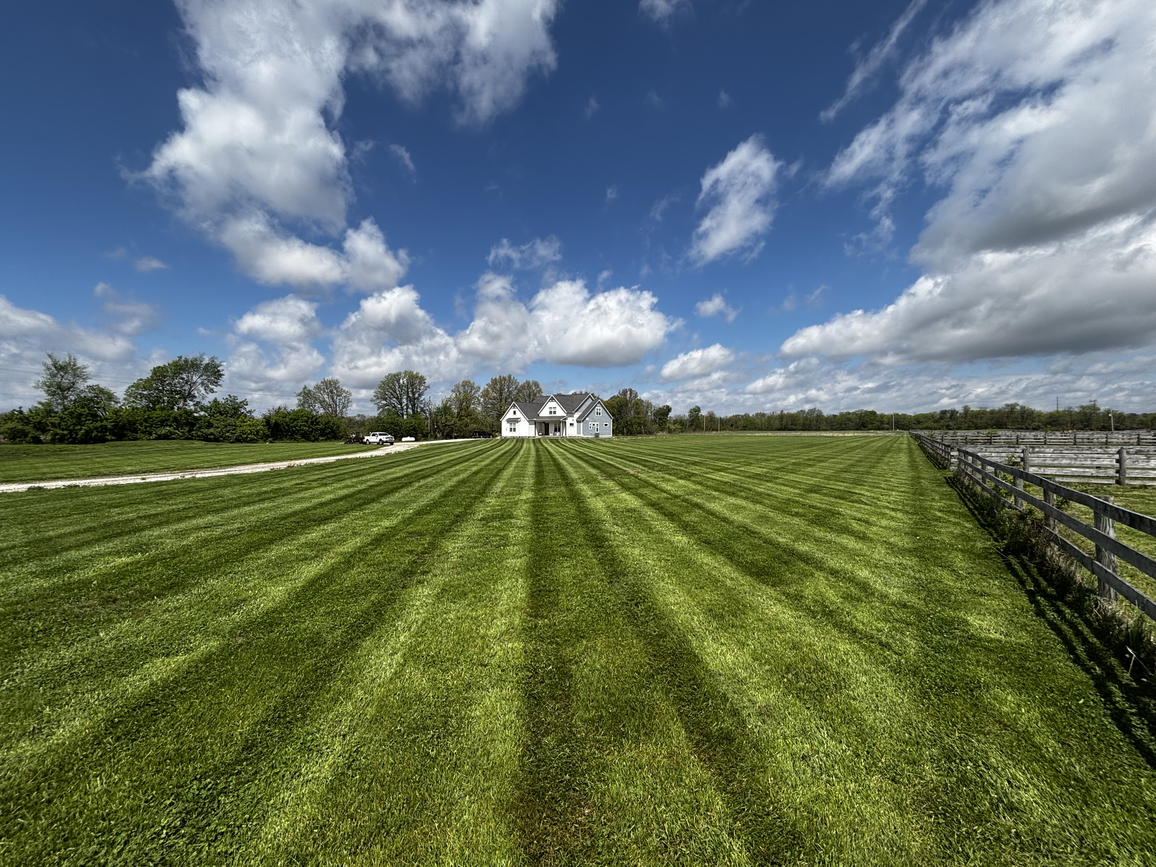 Expansive, perfectly striped vibrant green lawn extending to a rural home under a blue sky